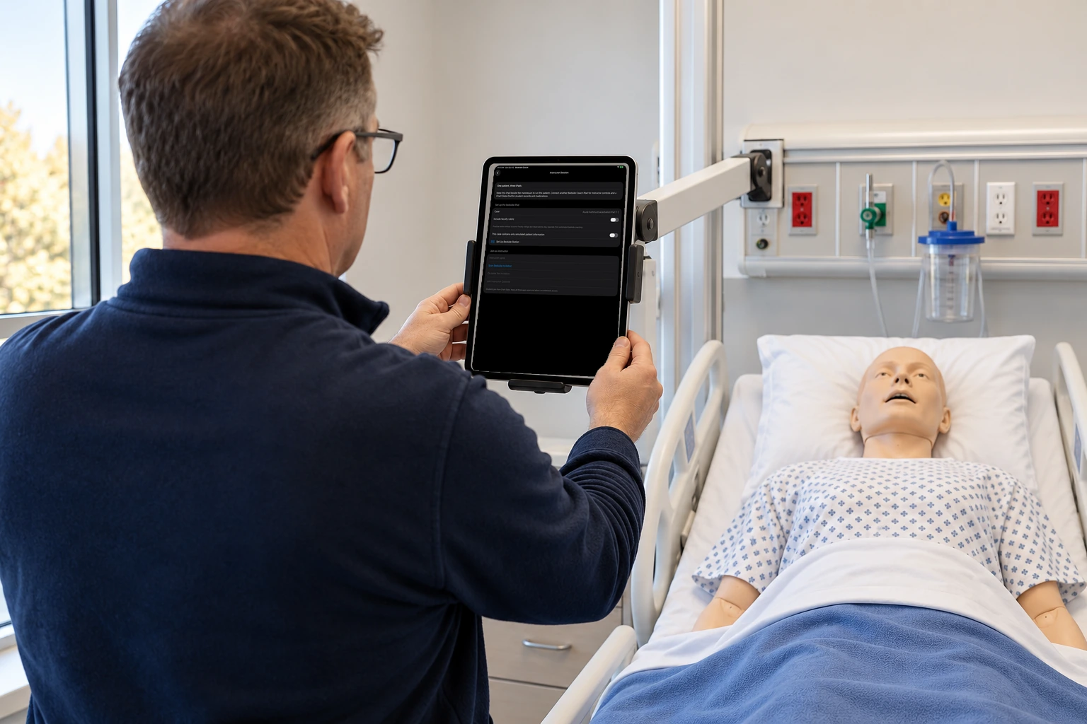 Faculty and a student stand by a manikin. The iPad shows the bedside station setup.